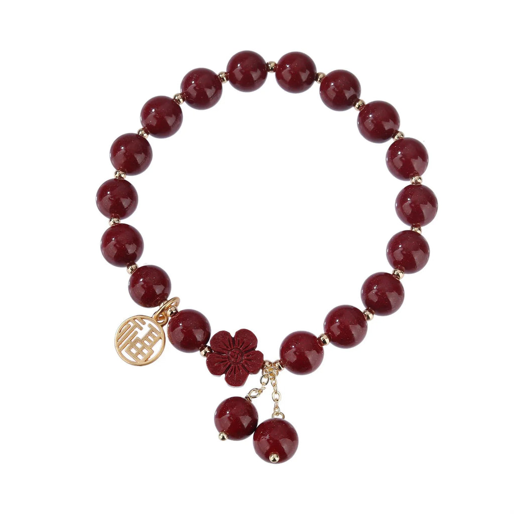 Handmade cinnabar bracelet with gold fu character and peach blossom tassel detail on white background