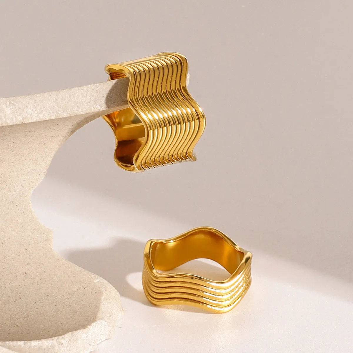 Stainless steel geometric wave pattern ring on a hand, showcasing its wide band and electroplated finish.