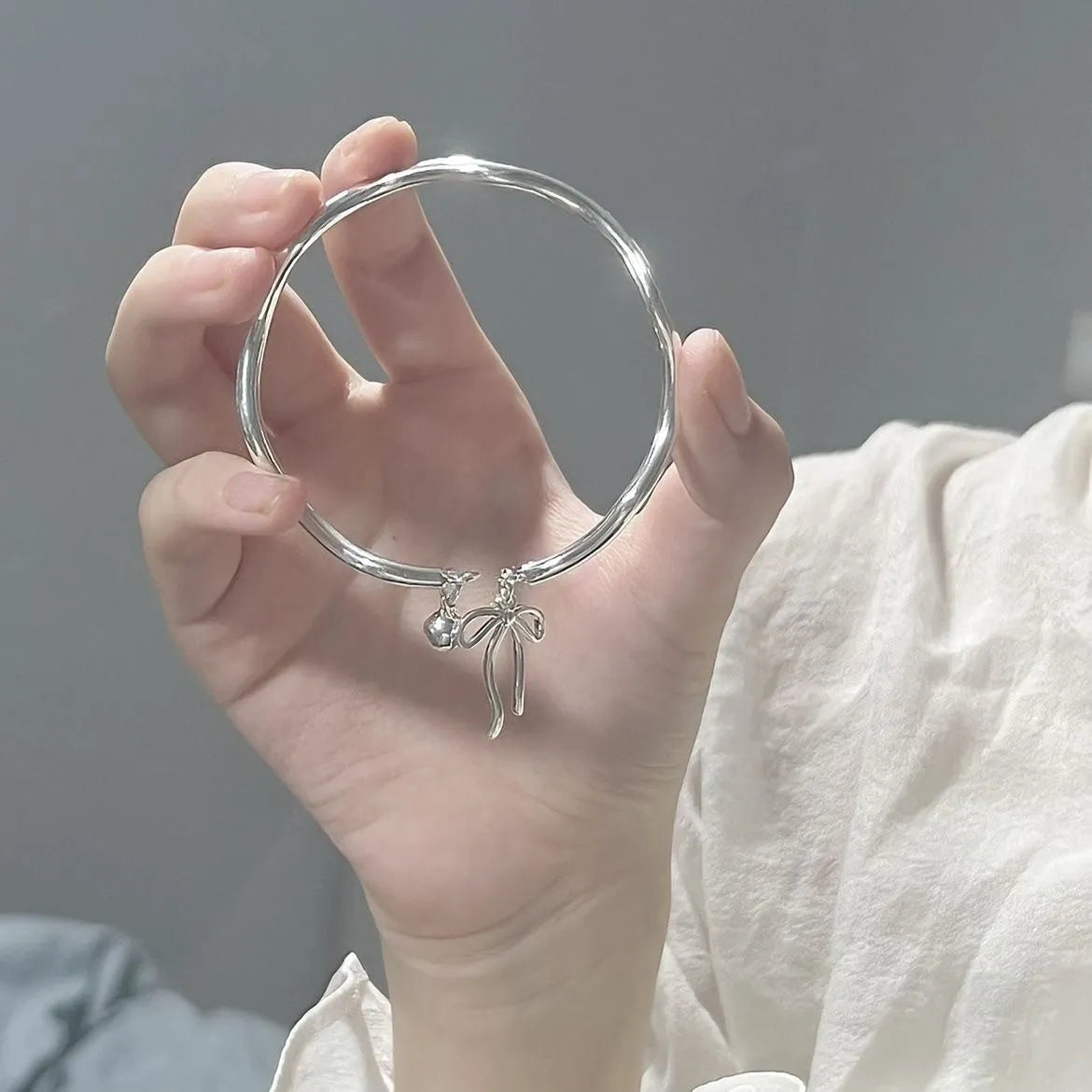 Silver tone adjustable bracelet with a bow and bell charm on a modelled wrist.