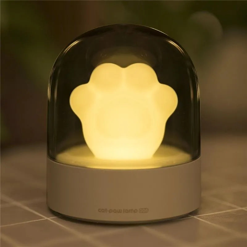 Grey or pink cat paw shaped USB rechargeable night light with music box on a desk.