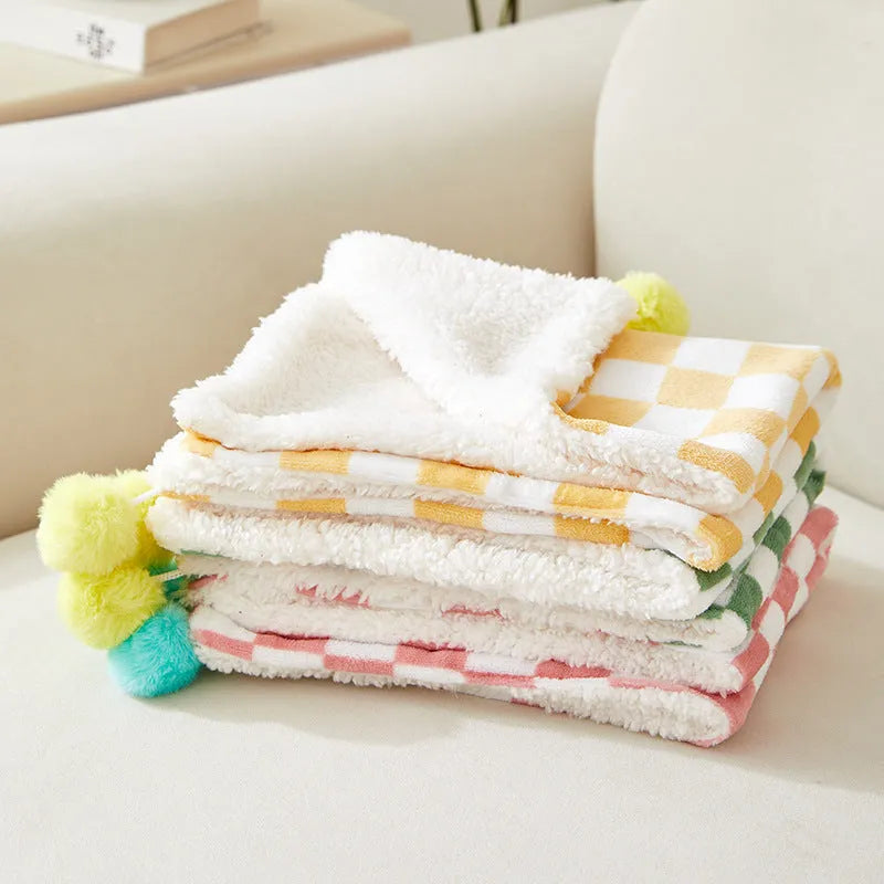 Green plaid pattern plush fleece pet blanket laid flat, showing soft texture and fur ball decoration.