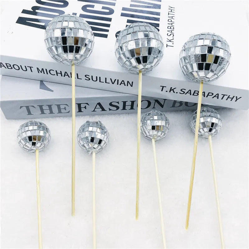 Glass mirror disco ball cake decoration on a wooden stick, showing reflective surface.