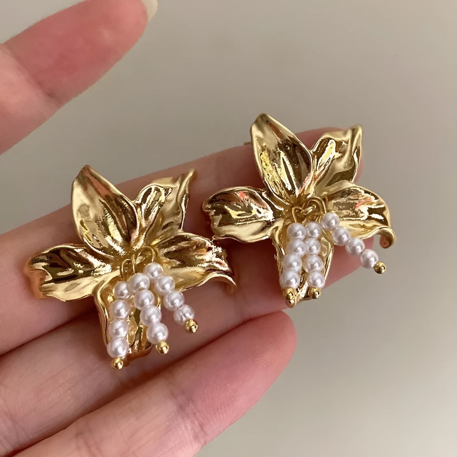 Gold pearl flower earrings with metal post back on white background, exaggerated floral shape