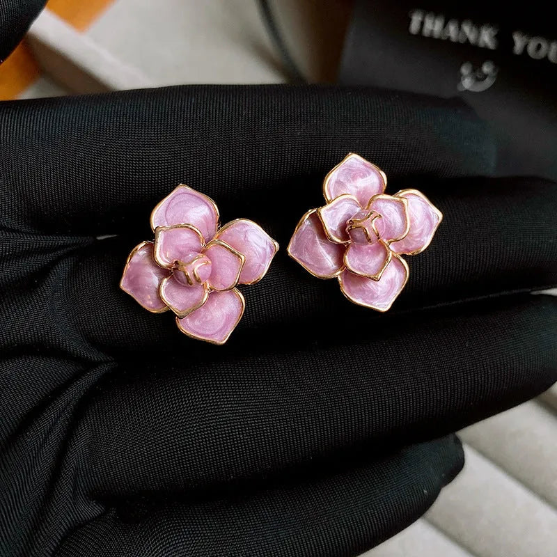A pair of purple and gold floral stud earrings with detailed needlework and an oil-spot glaze finish.