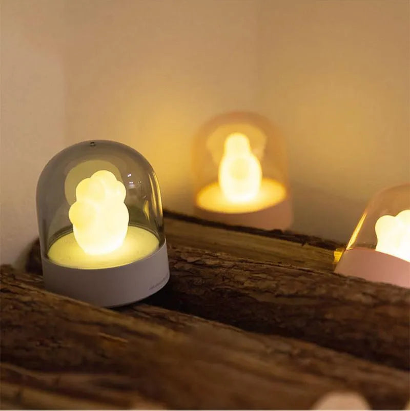 Grey or pink cat paw shaped USB rechargeable night light with music box on a desk.