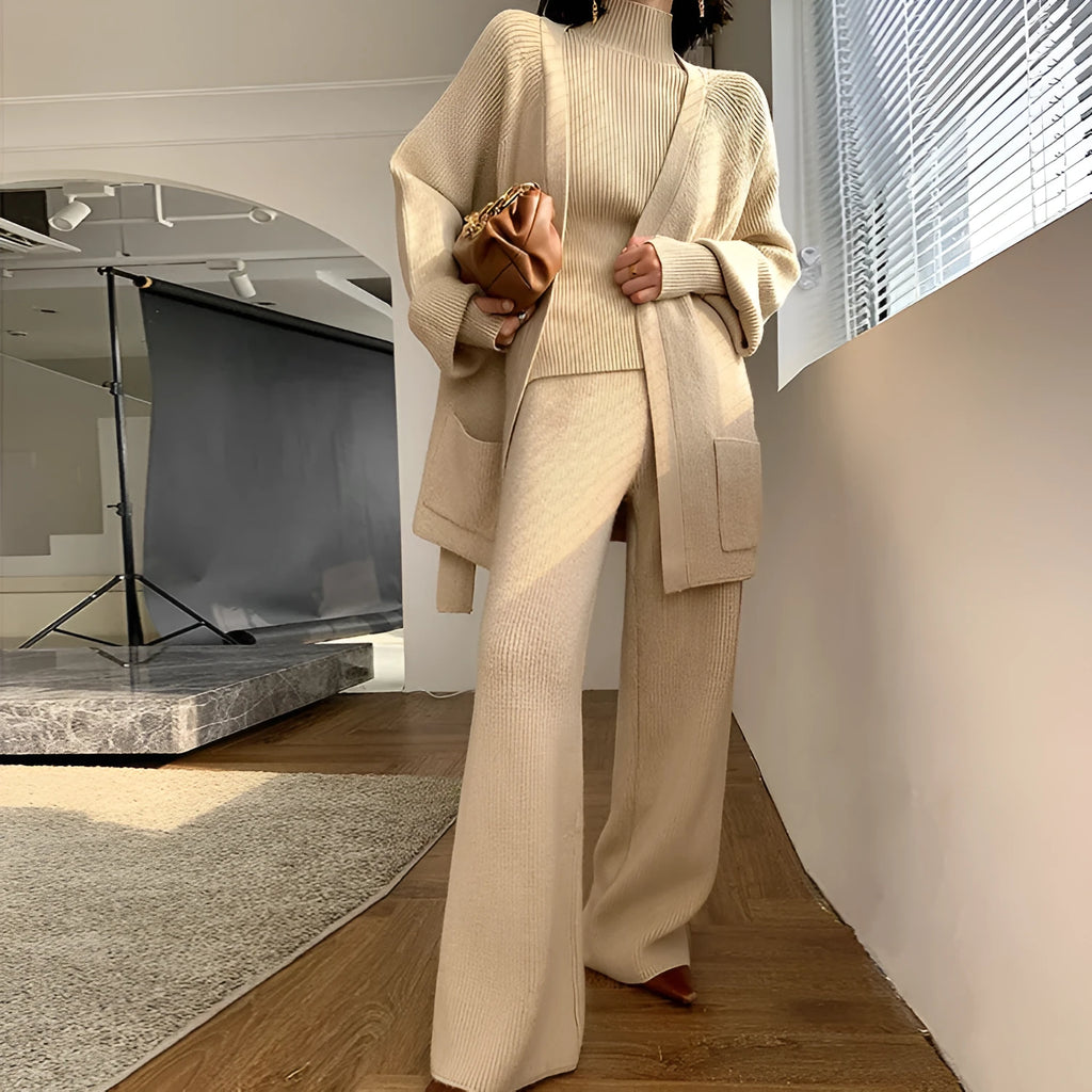 Women's knitted three-piece set showing apricot coloured wide-leg trousers, sweater, and cardigan with leather stitching