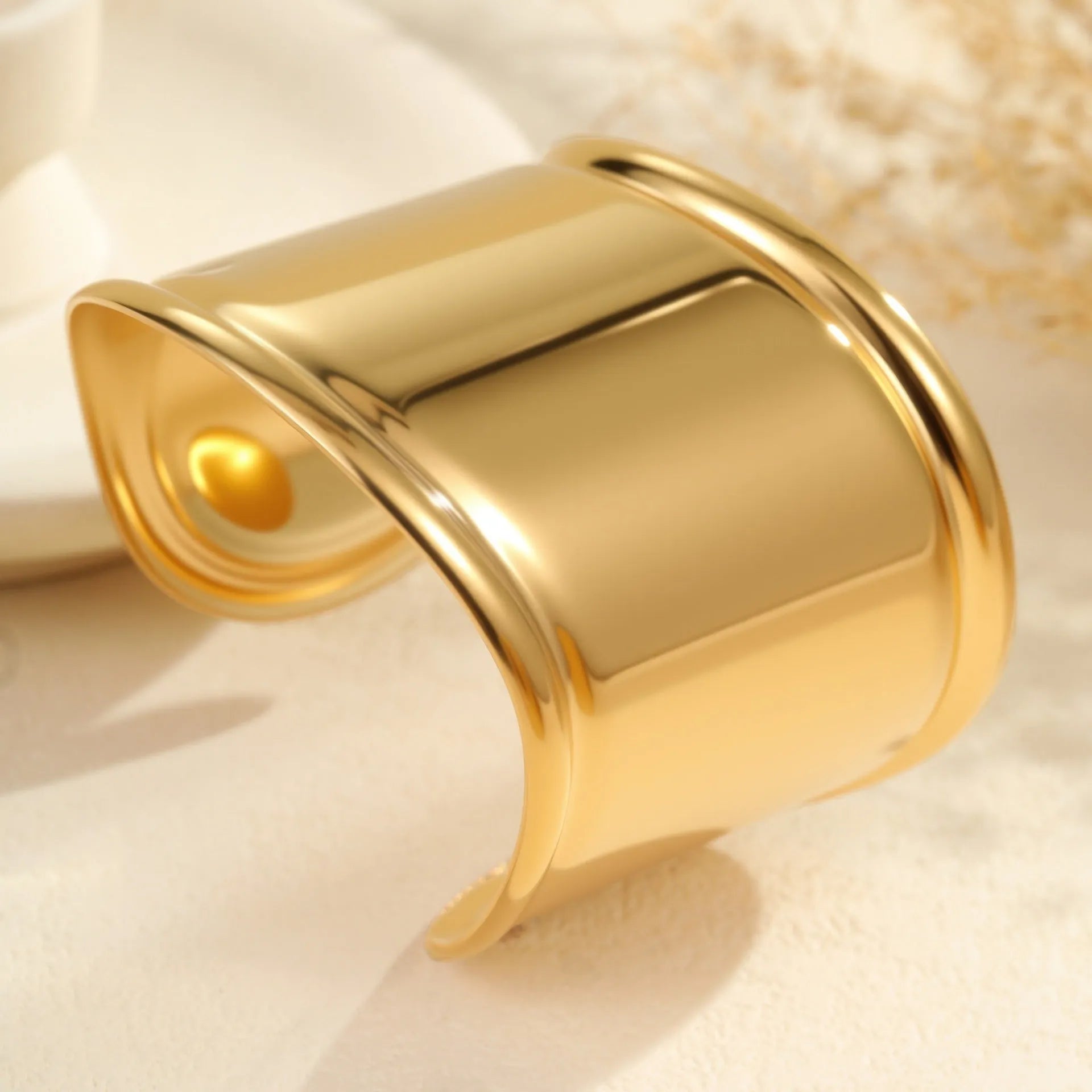 Wide geometric wave bracelet in gold-plated stainless steel on a woman's wrist.