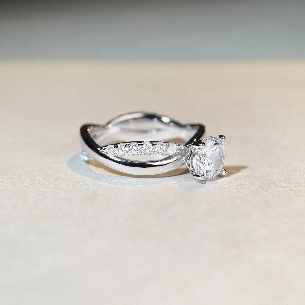 Silver moissanite ring with 1 carat stone, four-claw setting, and geometric cross design on a twisted arm band.