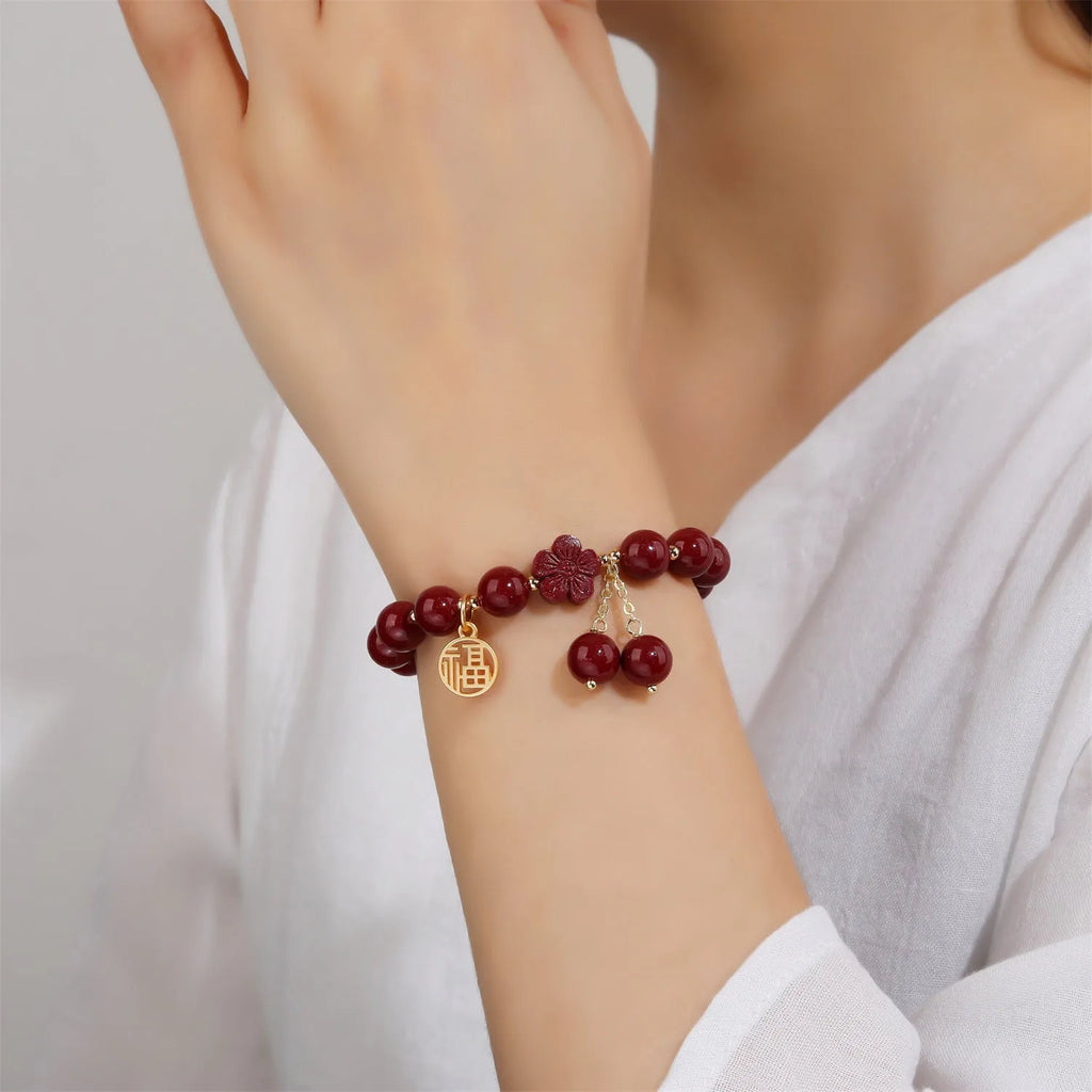 Handmade cinnabar bracelet with gold fu character and peach blossom tassel detail on white background
