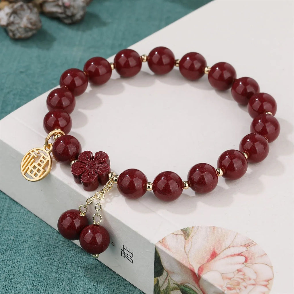 Handmade cinnabar bracelet with gold fu character and peach blossom tassel detail on white background