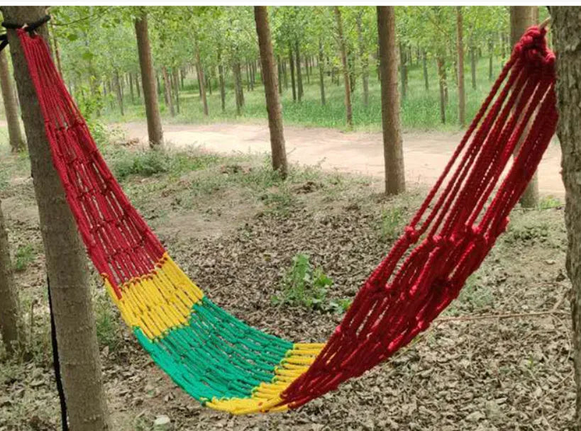 Nylon rope mesh outdoor hammock hung between two trees, showing its open weave and included tying ropes.