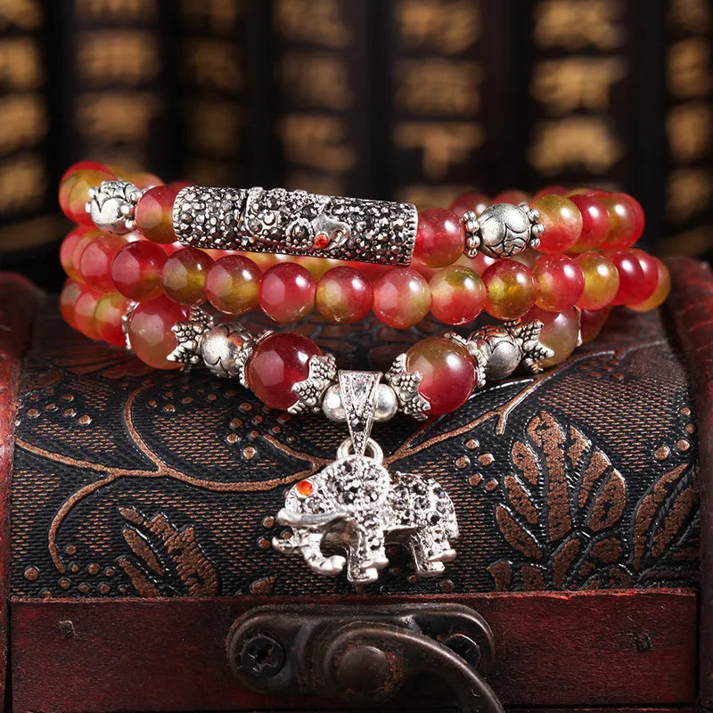 Close-up of a handmade watermelon crystal bracelet with a central Chinese knot and geometric beads.