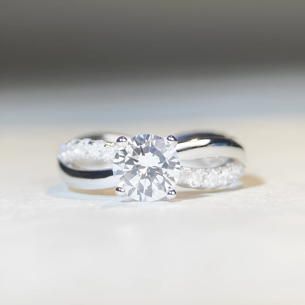 Silver moissanite ring with 1 carat stone, four-claw setting, and geometric cross design on a twisted arm band.