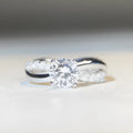 Silver moissanite ring with 1 carat stone, four-claw setting, and geometric cross design on a twisted arm band.