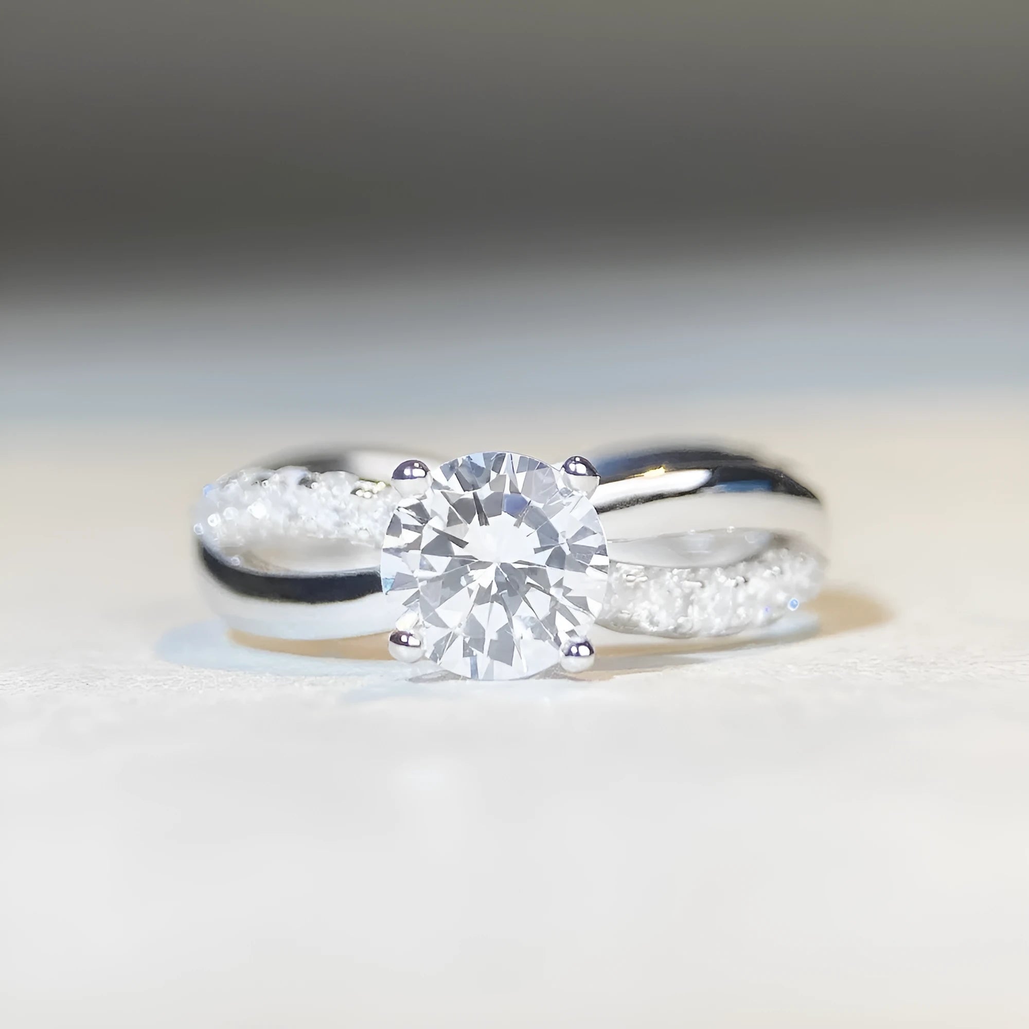 Silver moissanite ring with 1 carat stone, four-claw setting, and geometric cross design on a twisted arm band.