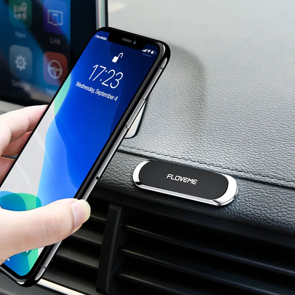 Black magnetic mobile phone holder with silver iron sheet and white foam glue pad on a desk surface