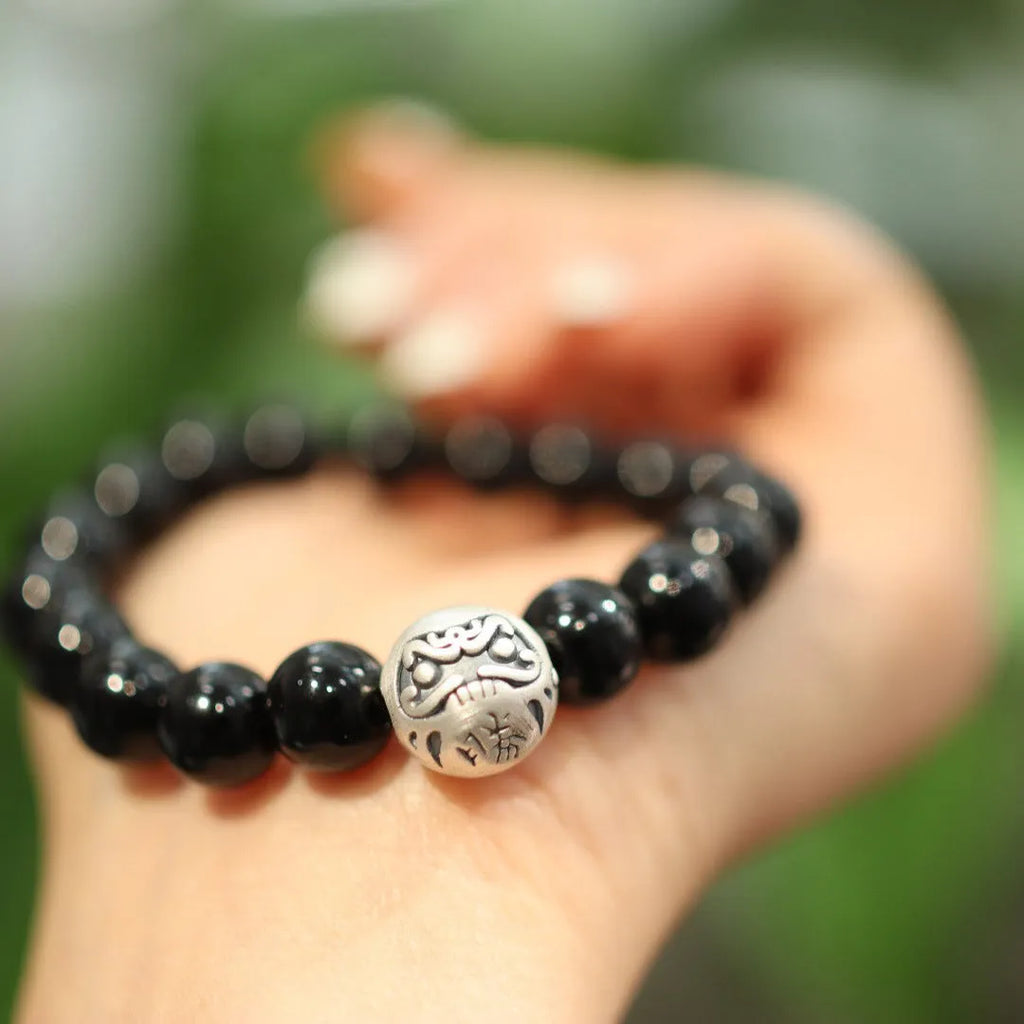 Close-up of a bracelet with large round black agate beads and sterling silver components on a wrist.