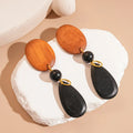 A pair of handcrafted wooden earrings with an elliptical shape in a silver, brown, and black colour finish.