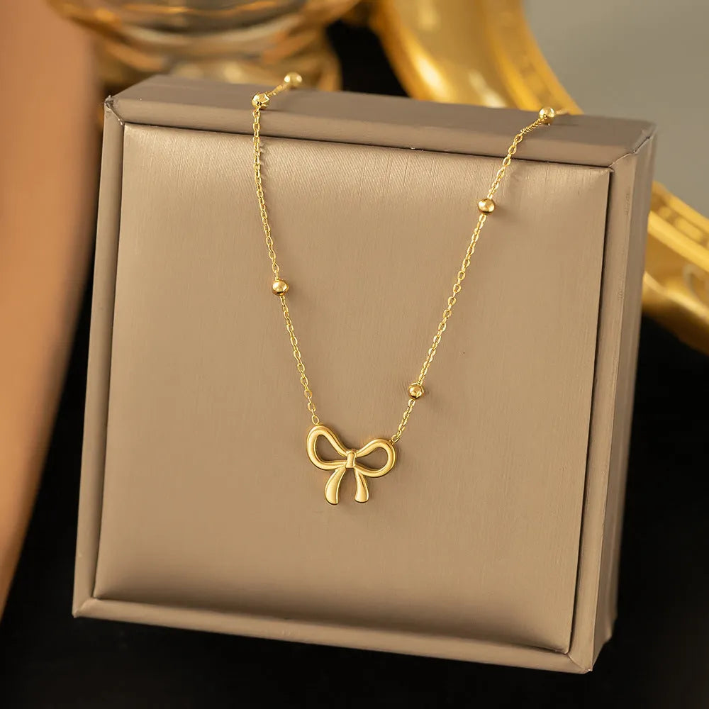 Gold-coloured titanium steel bow necklace with cross chain detail on white background