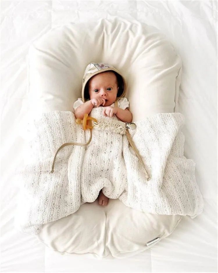 Beige portable baby nest cot cushion measuring 75cm by 45cm on a floor.