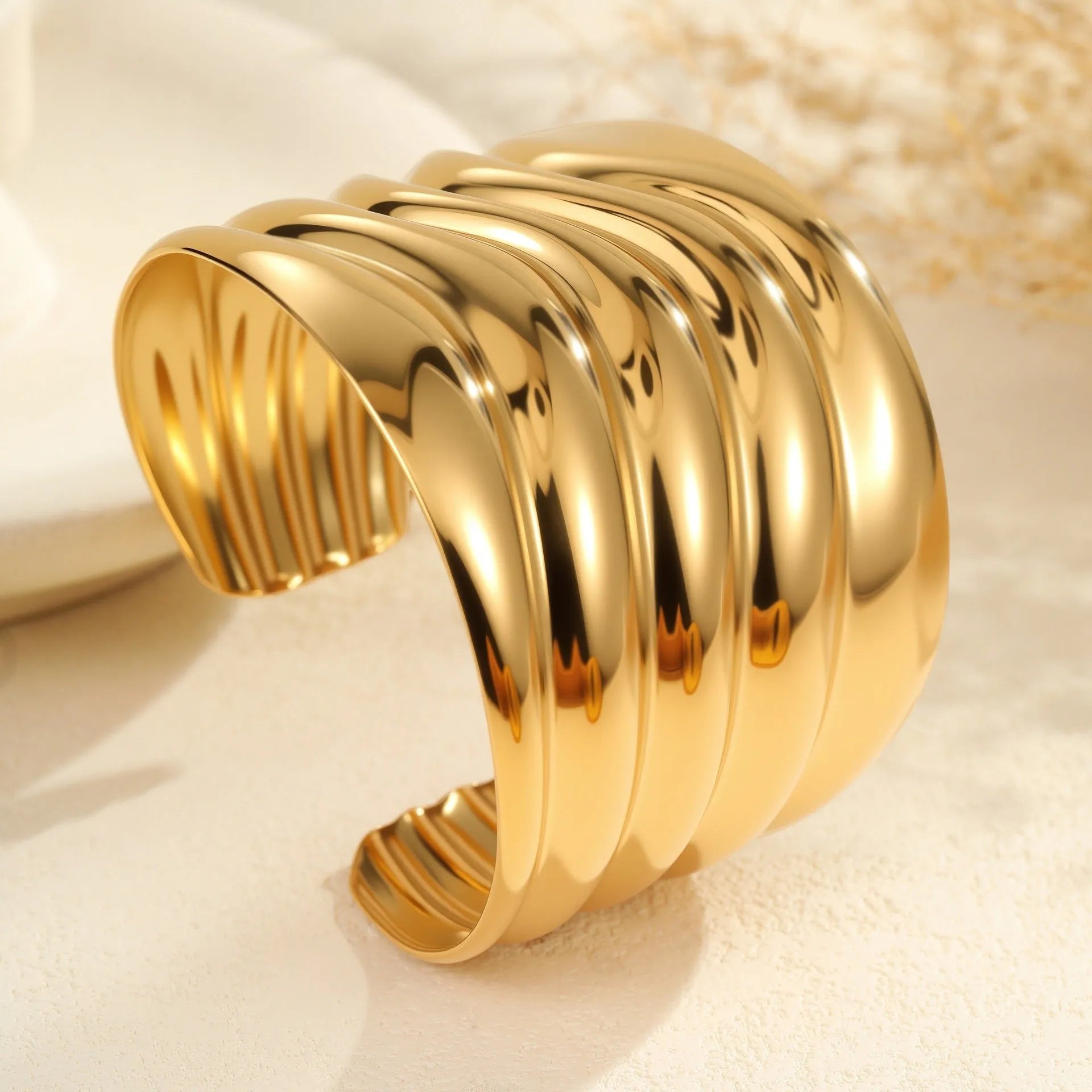 Wide geometric wave bracelet in gold-plated stainless steel on a woman's wrist.