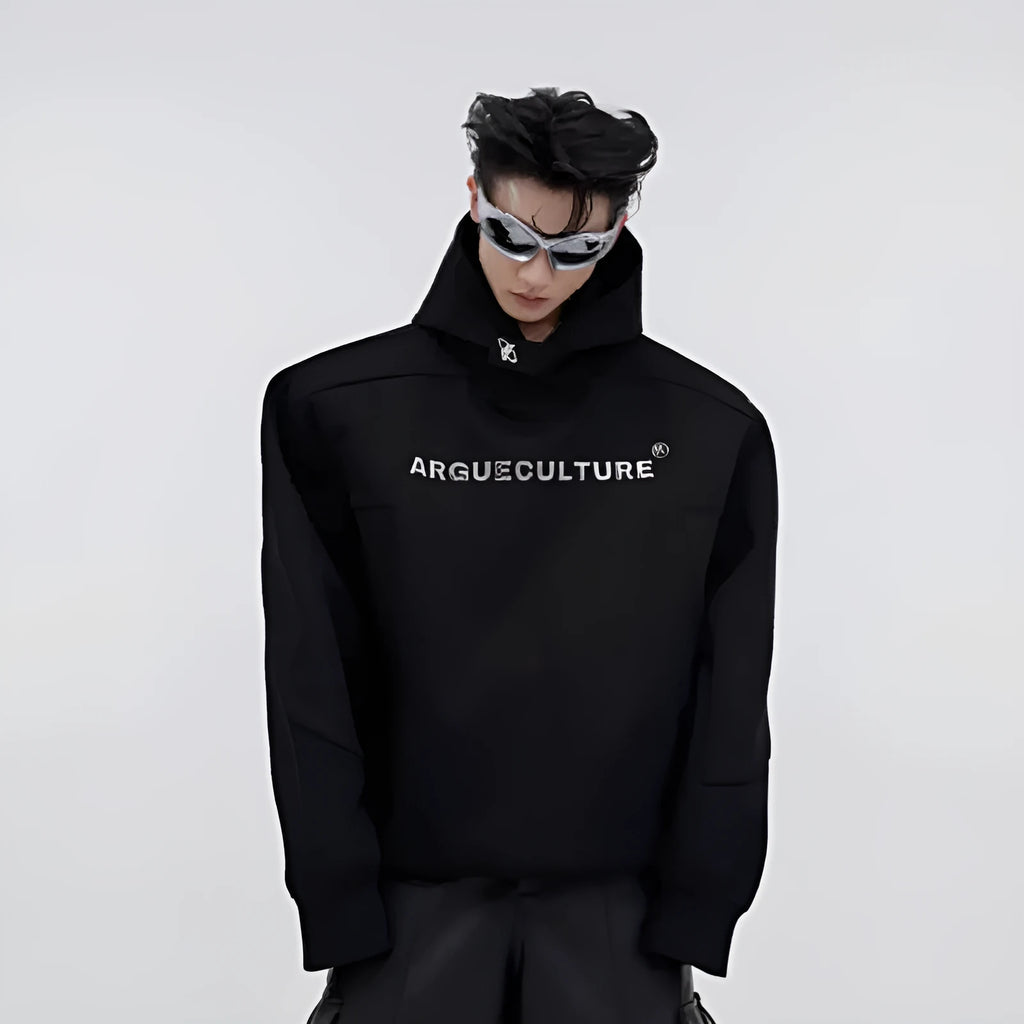 Man wearing a black loose-fit hooded sweater with heavy shoulder pads and a silver metallic graphic print on the chest.