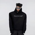 Man wearing a black loose-fit hooded sweater with heavy shoulder pads and a silver metallic graphic print on the chest.