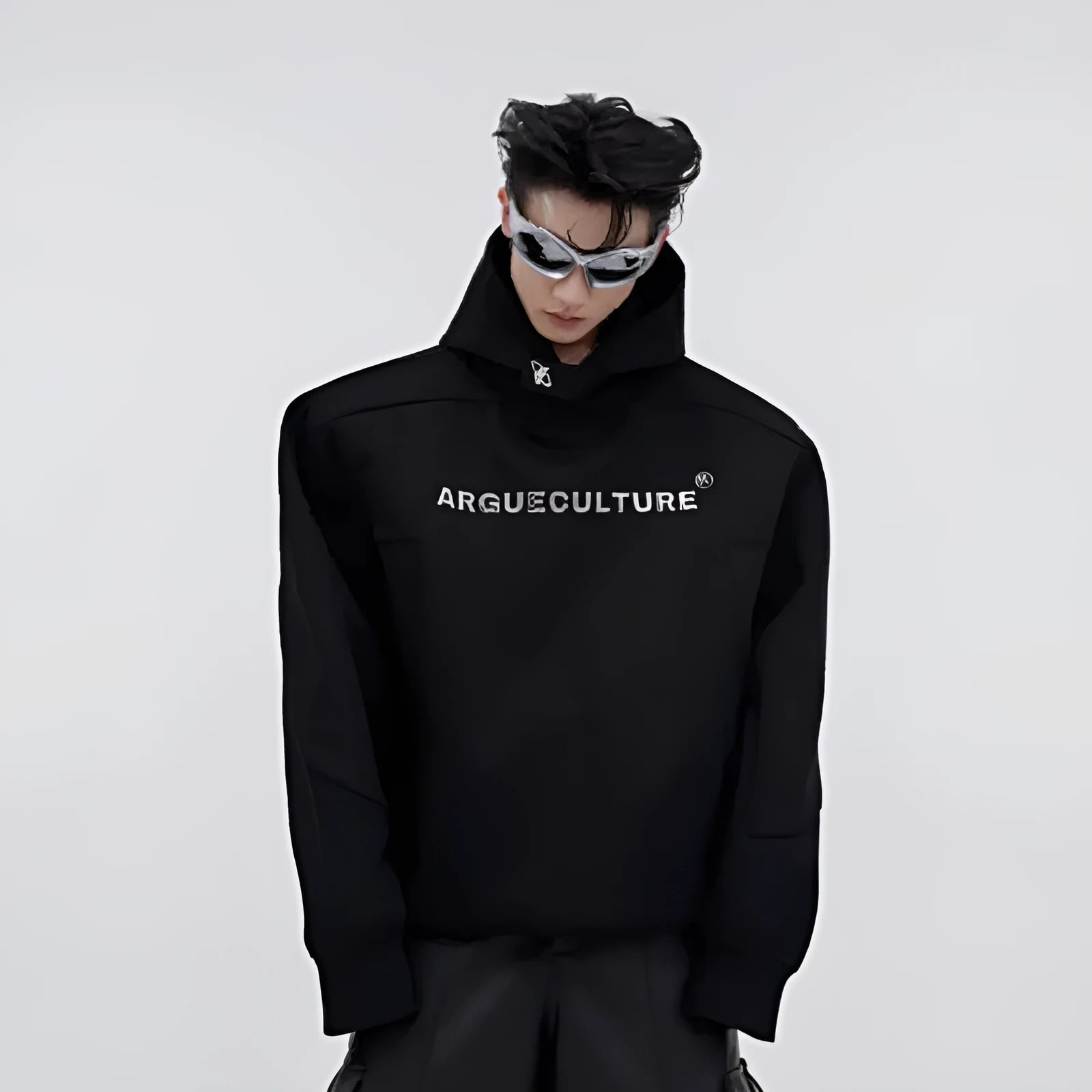 Man wearing a black loose-fit hooded sweater with heavy shoulder pads and a silver metallic graphic print on the chest.