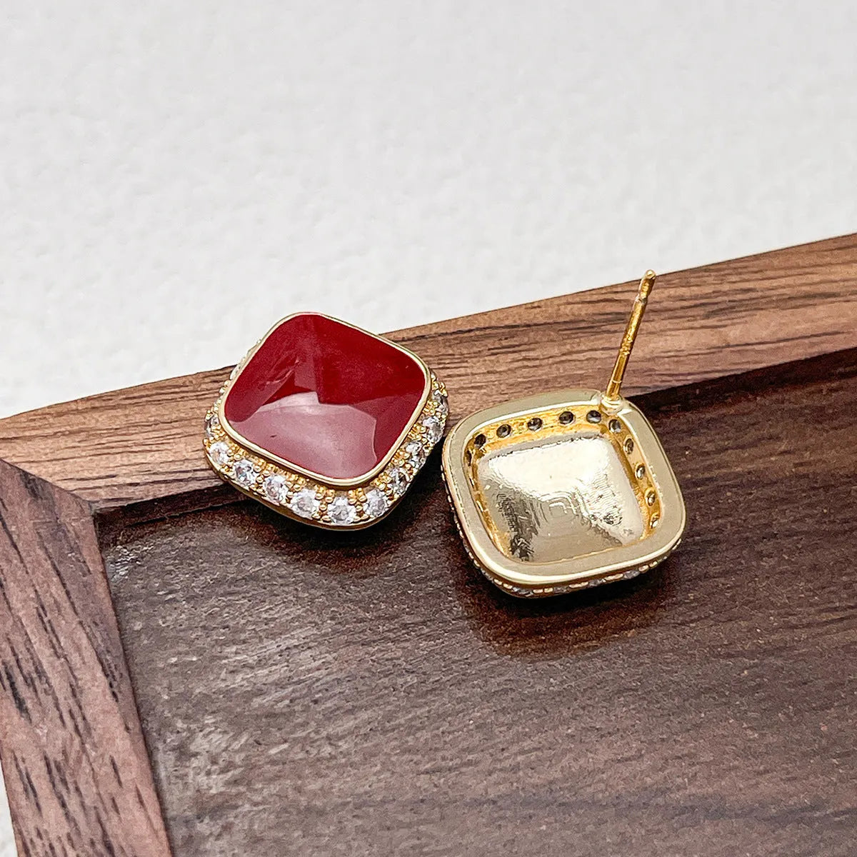 A pair of red geometric square alloy earrings with inlaid detailing on a white background.