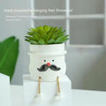 Cartoon style ceramic hanging foot succulent planter on a desktop.