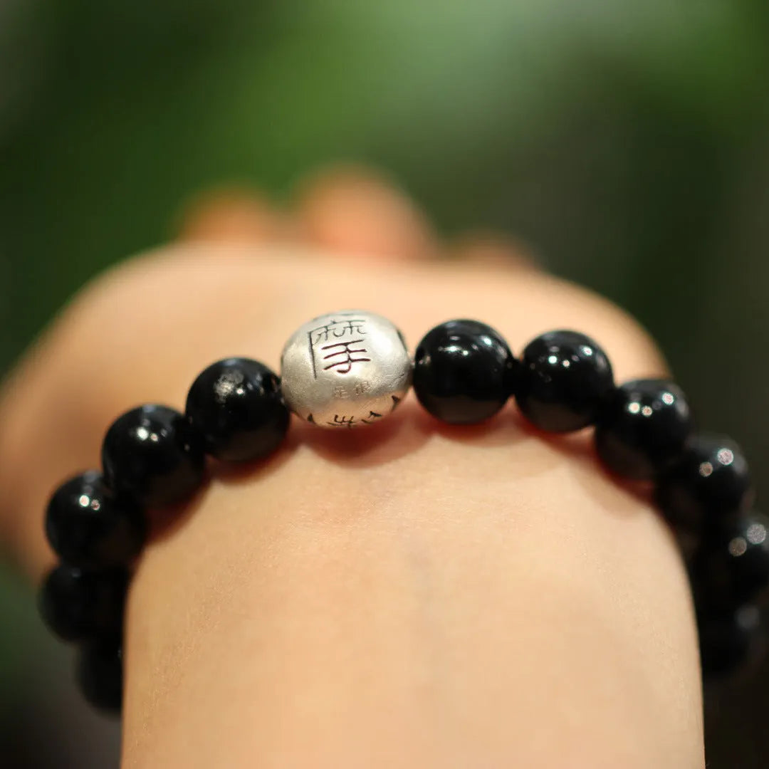 Close-up of a bracelet with large round black agate beads and sterling silver components on a wrist.