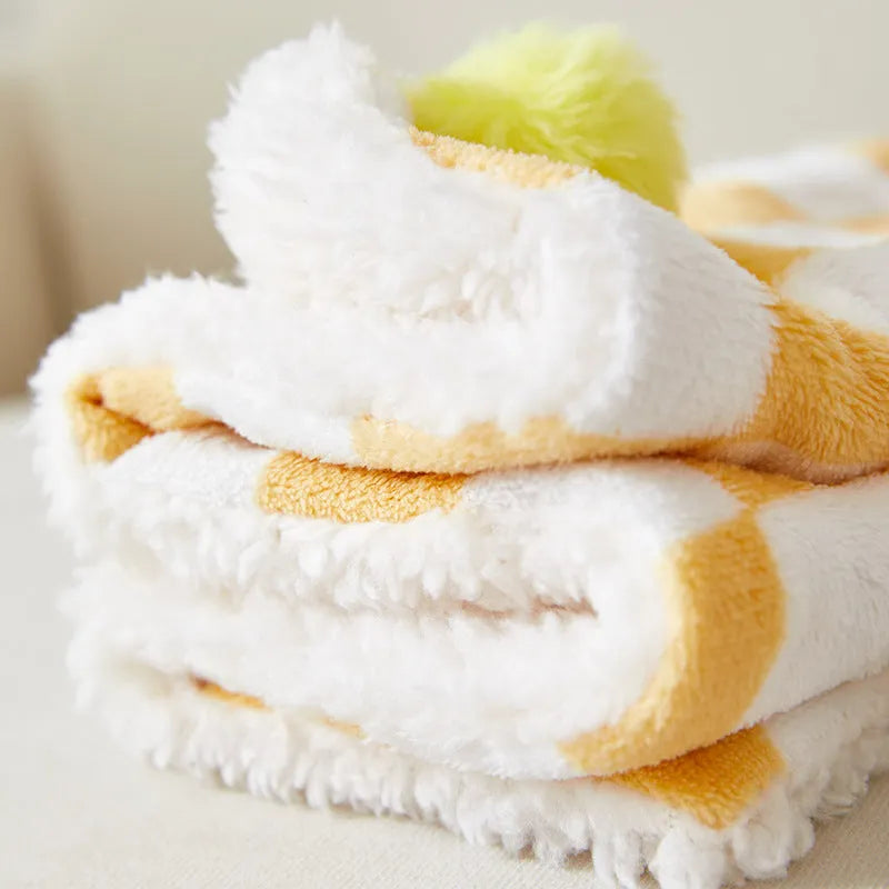 Green plaid pattern plush fleece pet blanket laid flat, showing soft texture and fur ball decoration.