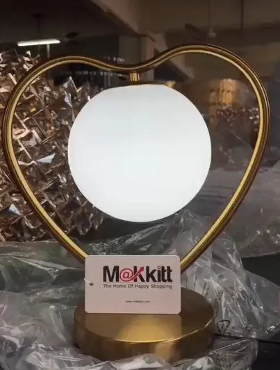 Heart shaped decorative LED lamp with polyresin base and frosted acrylic shade on a table.