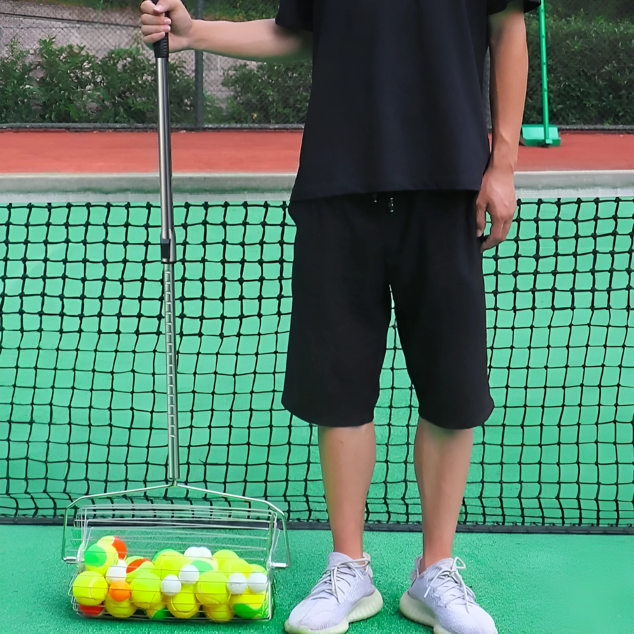Stainless steel tennis ball picker roller on a court next to tennis balls.