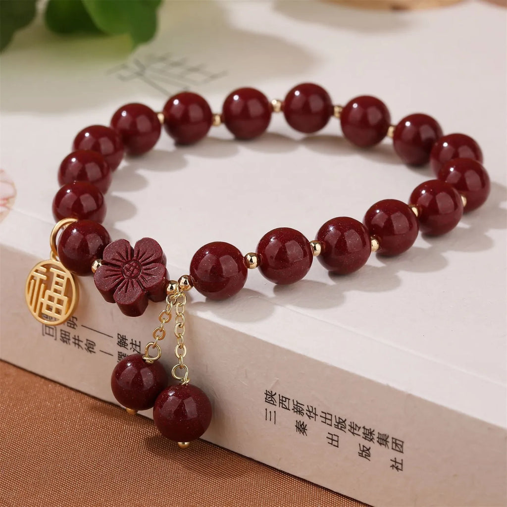 Handmade cinnabar bracelet with gold fu character and peach blossom tassel detail on white background