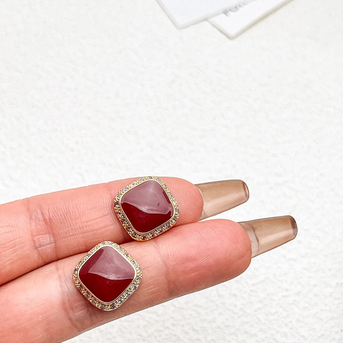 A pair of red geometric square alloy earrings with inlaid detailing on a white background.
