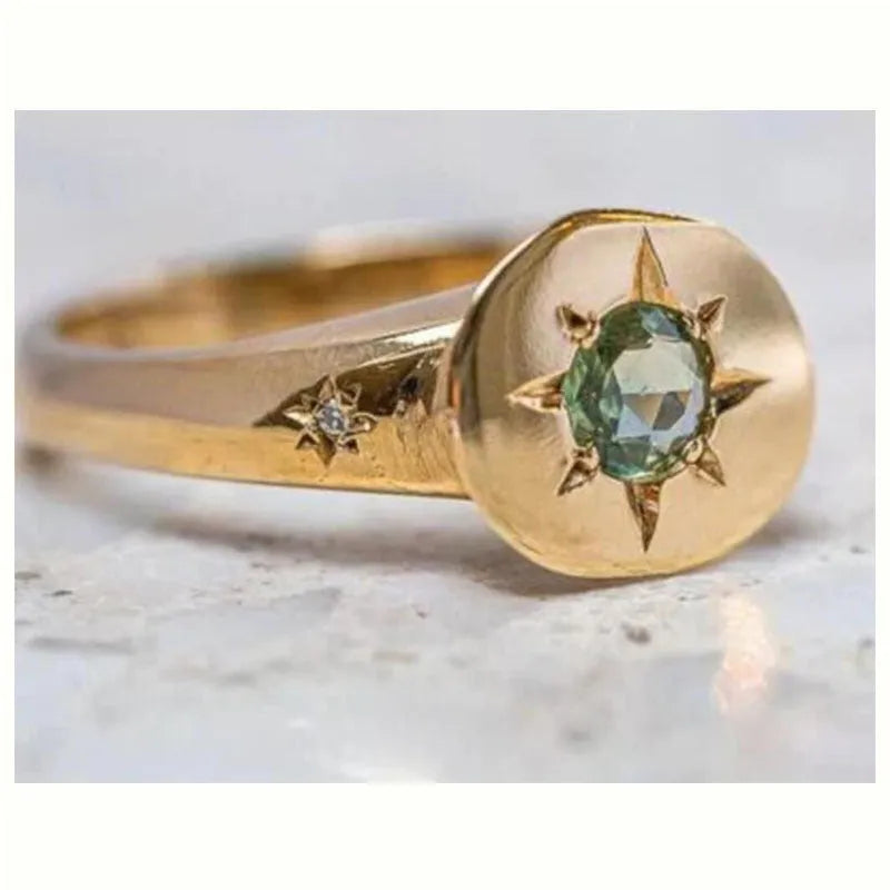 Gold coloured oval star zircon ring with adjustable opening on a plain background.