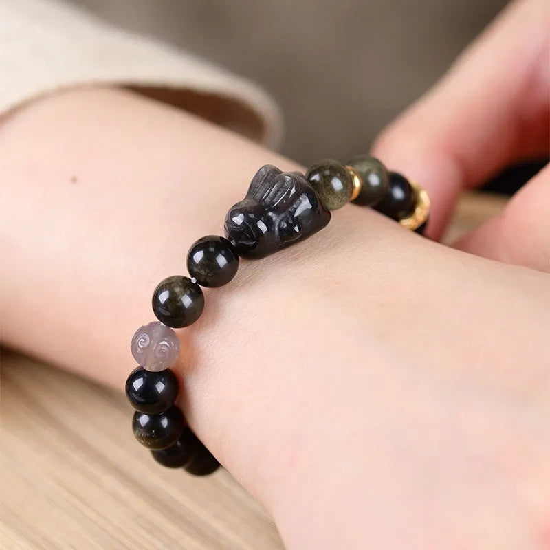 Handmade unisex lying rabbit Jin Yaoshi obsidian bracelet with gray agate and brass beads on neutral background