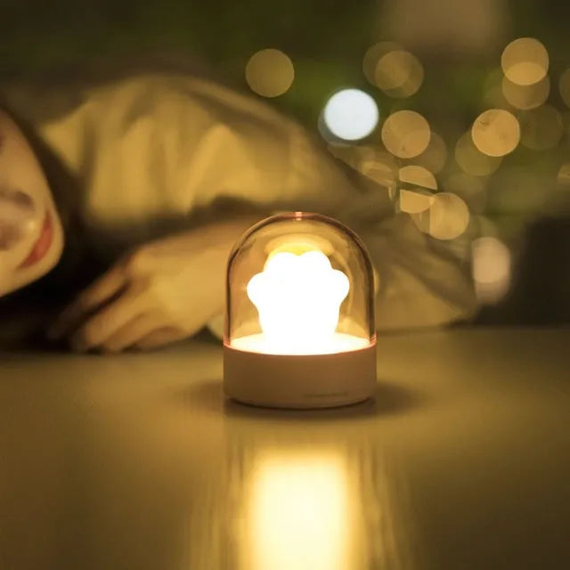 Grey or pink cat paw shaped USB rechargeable night light with music box on a desk.