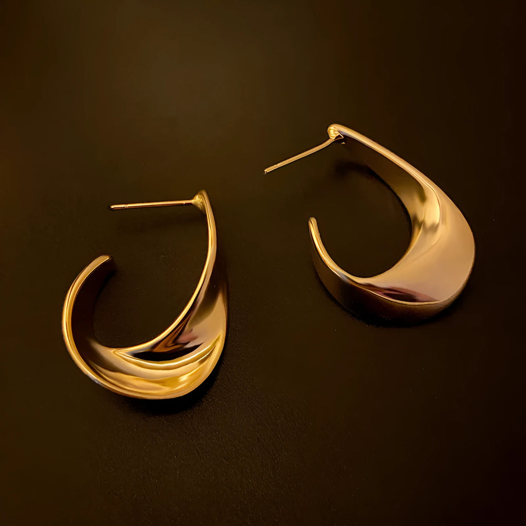 Close-up of gold twisted geometric metal earrings with a round design element.