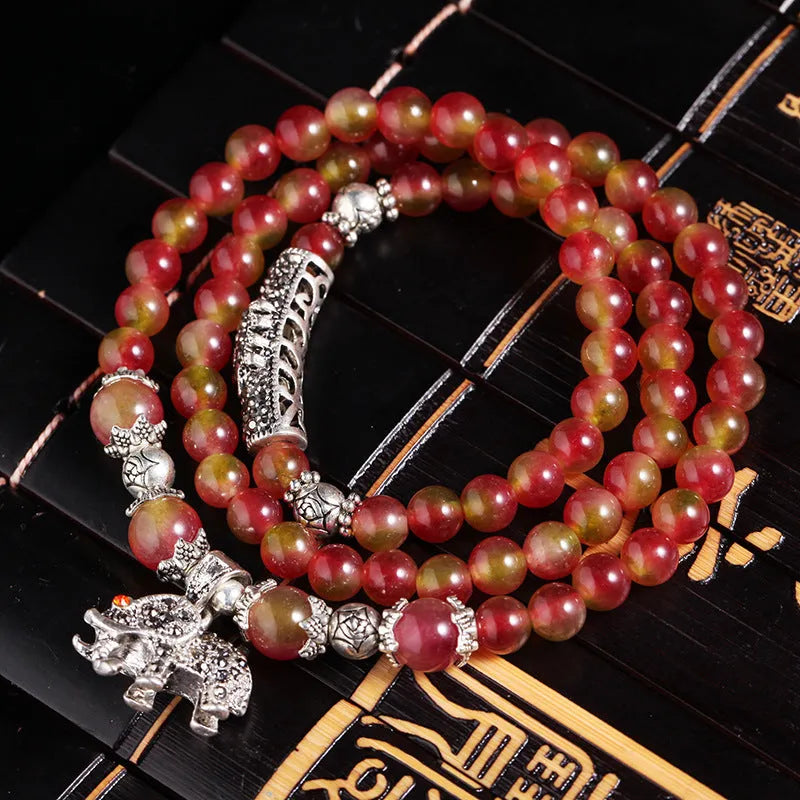 Close-up of a handmade watermelon crystal bracelet with a central Chinese knot and geometric beads.