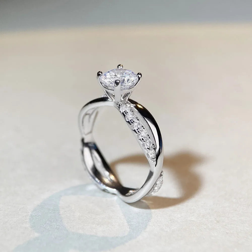 Silver moissanite ring with 1 carat stone, four-claw setting, and geometric cross design on a twisted arm band.