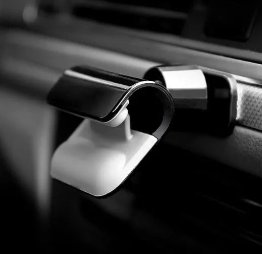 Black gravity car phone holder with 360-degree rotating bracket mounted on a car dashboard holding a mobile phone.