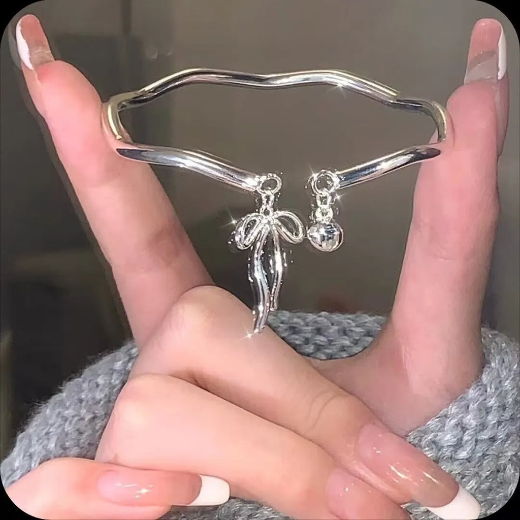 Silver tone adjustable bracelet with a bow and bell charm on a modelled wrist.