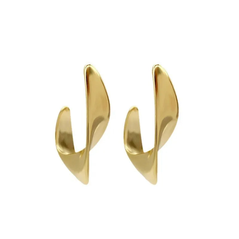 Close-up of gold twisted geometric metal earrings with a round design element.