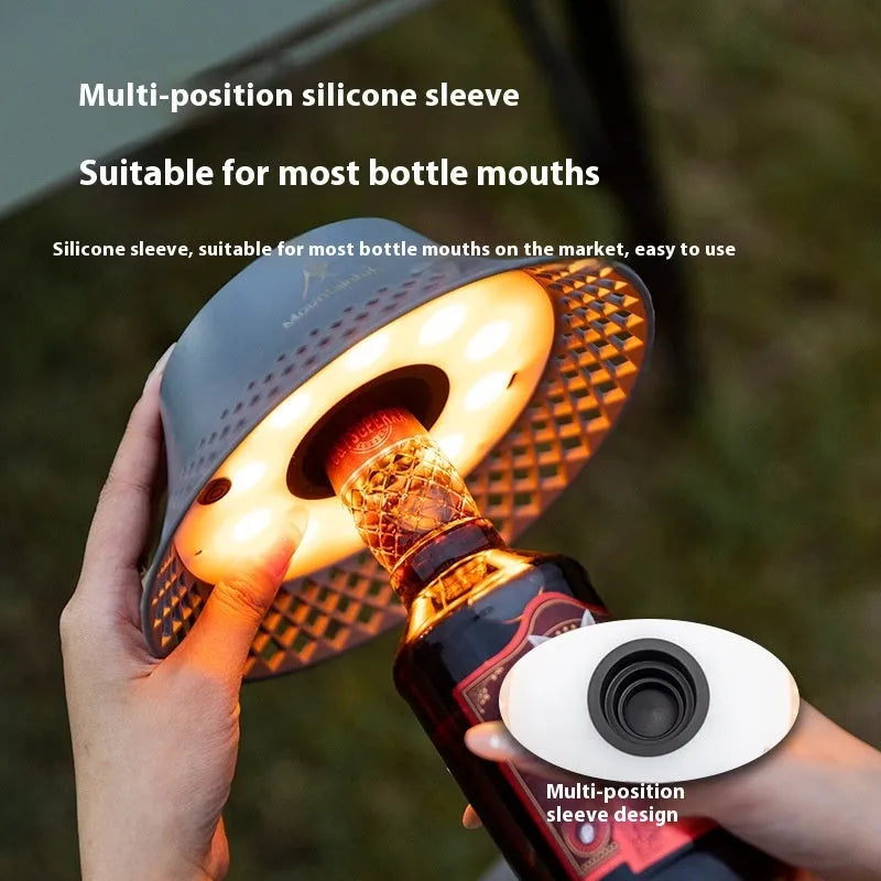 Beige wine bottle shaped camping lantern with USB-C port, shown lit on a wooden table outdoors.