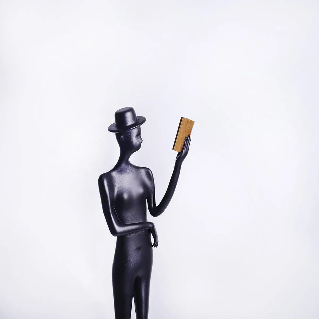 Black cast aluminium sculpture of a woman reading, 51cm tall on a desk.