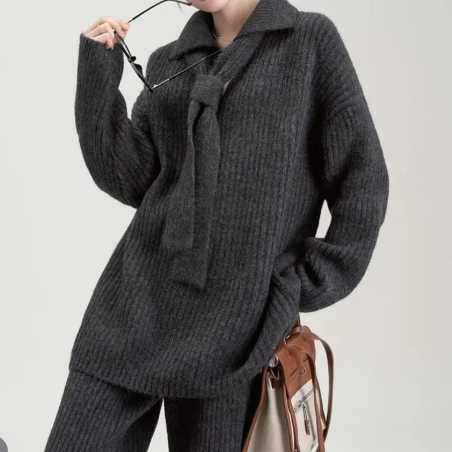 Dark gray knitted sweater and trousers two-piece set laid flat, showing long sleeves and elegant stitching details.