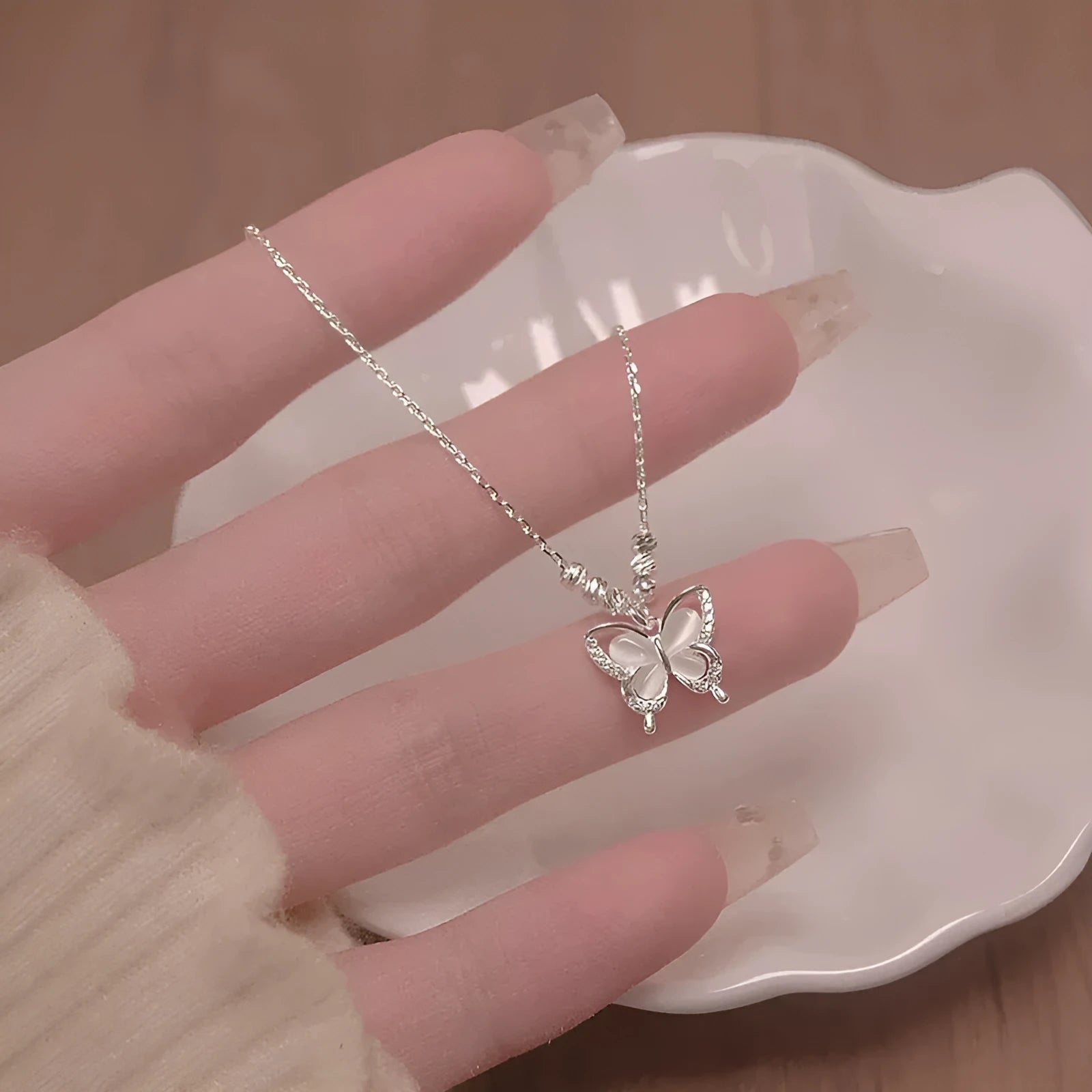 A silver necklace with a butterfly pendant on a cross chain, showing adjustable length.