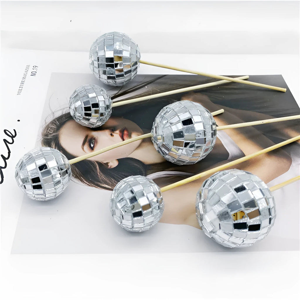 Glass mirror disco ball cake decoration on a wooden stick, showing reflective surface.